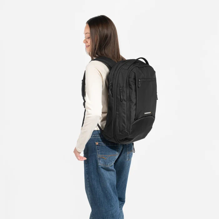 A woman wearing a Sherpani Crew Raven Black Travel Backpack on her back against a white background.  #color_raven-black