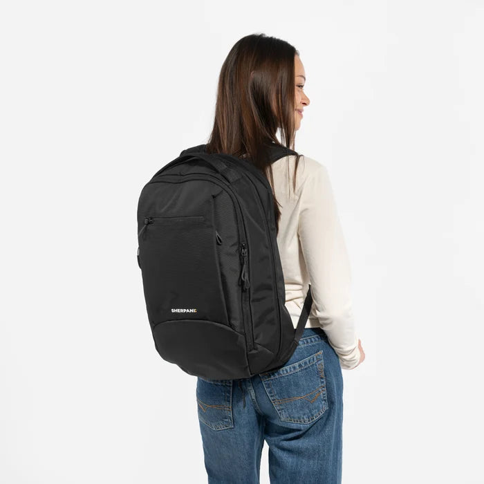 A woman wearing a Sherpani Crew Raven Black Travel Backpack on her back against a white background. #color_raven-black