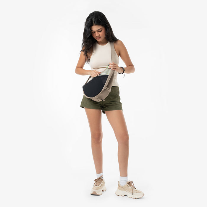 Woman wearing a Sherpani Cross Link Desert Aloe Adventure Sling across her body against white backdrop. #color_desert-aloe