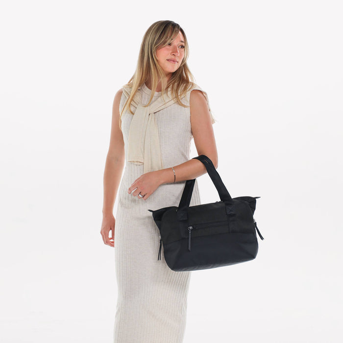 Woman holding a Sherpani Eclipse Carbon Expandable Tote by handheld straps against white backdrop.  #color_carbon