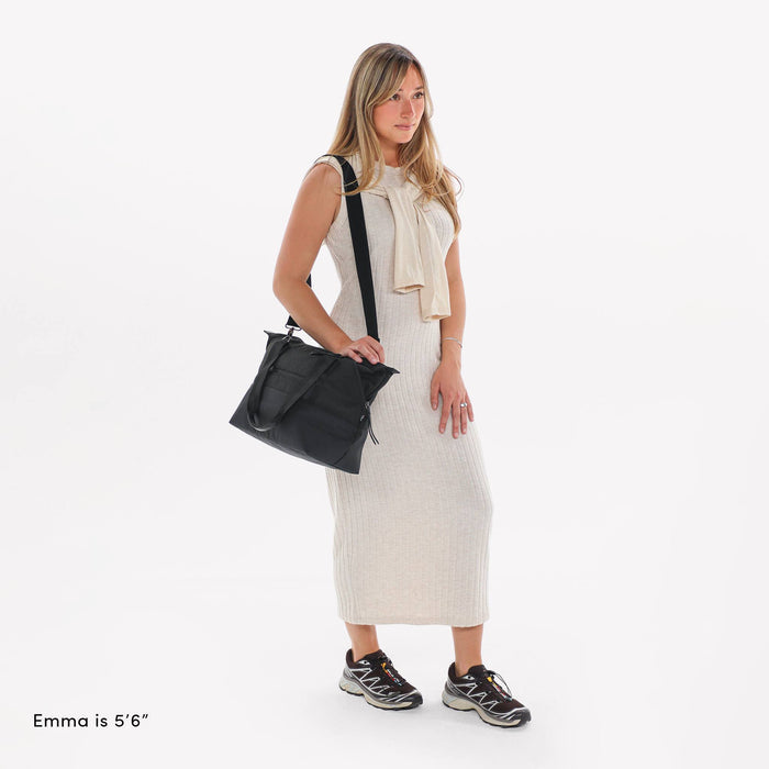 Woman wearing a Sherpani Eclipse Carbon Expandable Tote by crossbody strap against white backdrop.  #color_carbon