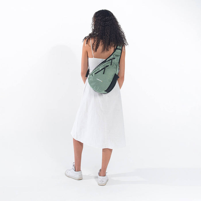 A woman wearing a Sherpani Esprit Aloe Mist Green Anti-theft Sling Bag on her back against a white background. #color_aloe-mist-green