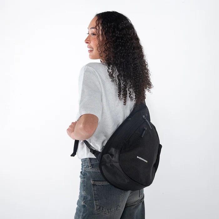 Woman wearing a Sherpani Esprit Carbon Black Anti-theft Sling on her back against white backdrop. #color_carbon-black