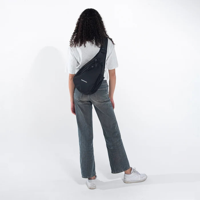 Woman wearing a Sherpani Esprit Carbon Black Anti-theft Sling on her back against white backdrop. #color_carbon-black