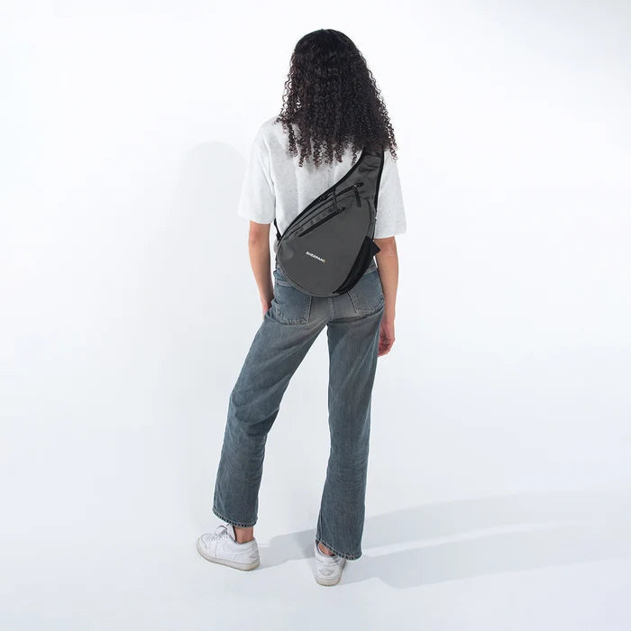 Woman wearing a Sherpani Esprit Granite  Anti-theft Sling on her back against white backdrop.  #color_granite-grey