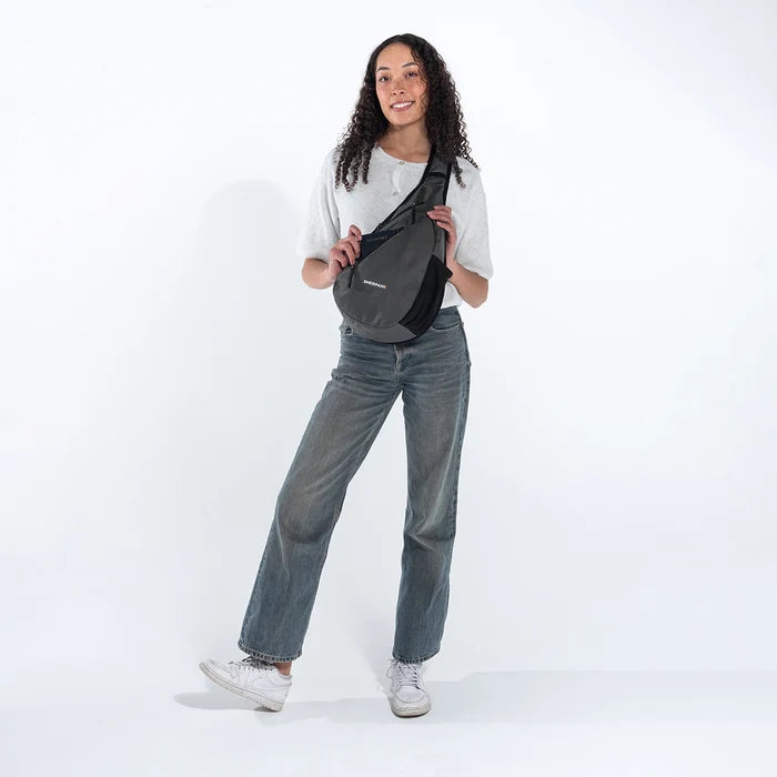 Woman wearing a Sherpani Esprit Granite  Anti-theft Sling on her front with a passport in main pocket against white backdrop.  #color_granite-grey