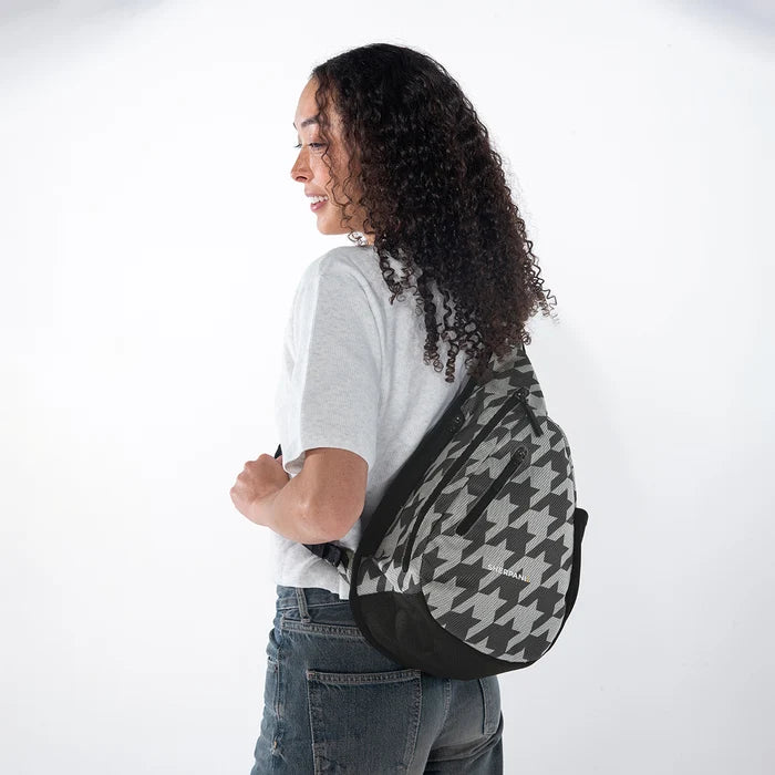 Woman wearing a Sherpani Esprit Houndstooth Anti-theft Sling on her back against white backdrop.  #color_houndstooth-print
