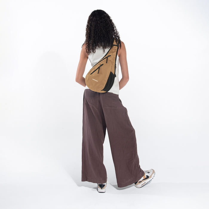 Woman wearing a Sherpani Esprit Sand Anti-theft Sling on her back against white backdrop. #color_sand-tan