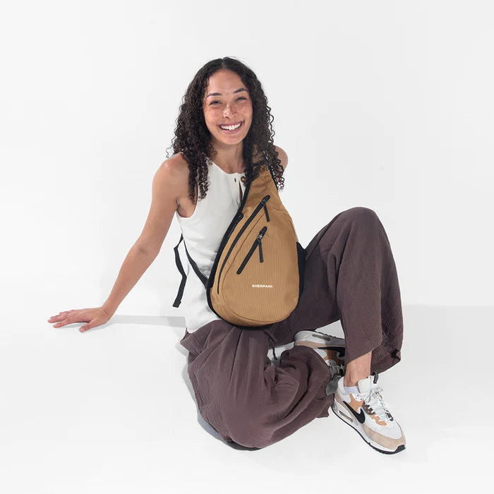 Woman wearing a Sherpani Esprit Sand Anti-theft Sling on her front against white backdrop. #color_sand-tan