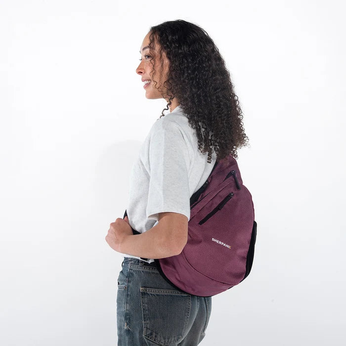 Woman wearing a Sherpani Esprit Smoky Orchid Anti-theft Sling on her back against white backdrop. #color_smoky-orchid-pink