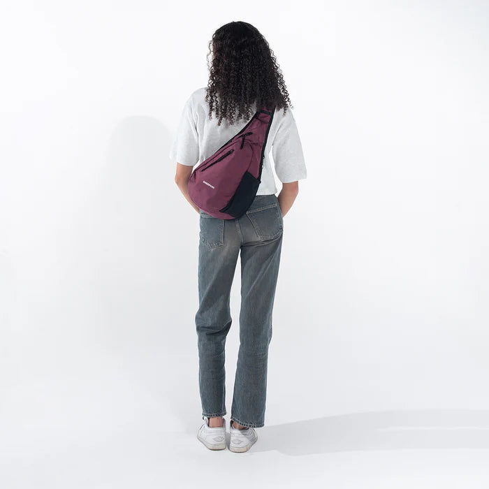 Woman wearing a Sherpani Esprit Smoky Orchid Anti-theft Sling on her back against white backdrop. #color_smoky-orchid-pink