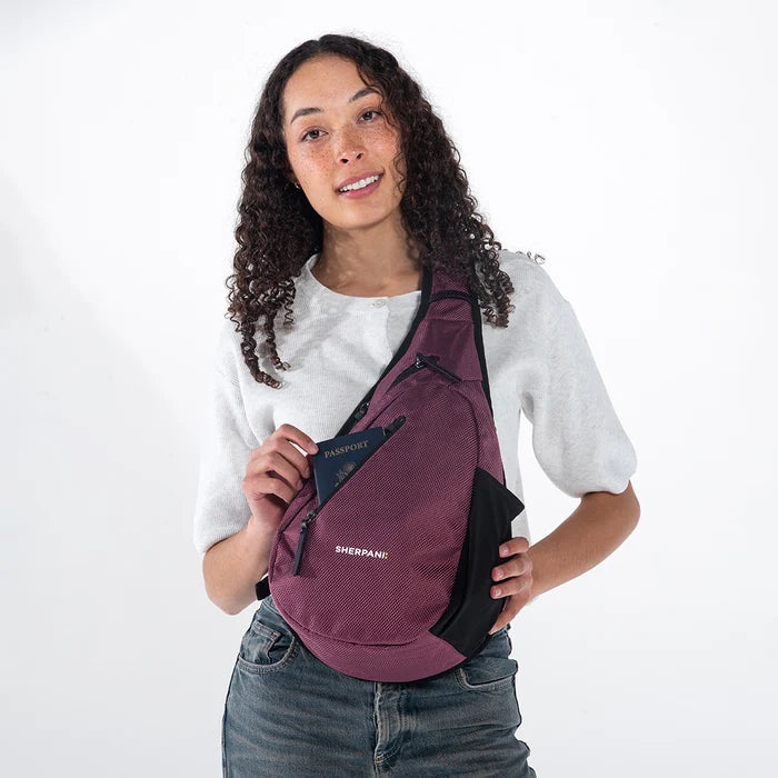 Woman wearing a Sherpani Esprit Smoky Orchid Anti-theft Sling on her front against white backdrop. #color_smoky-orchid-pink