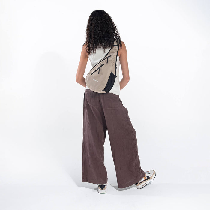 A woman wearing a Sherpani Esprit Straw Beige Anti-theft Sling Bag on her back against a white background. #color_straw-beige