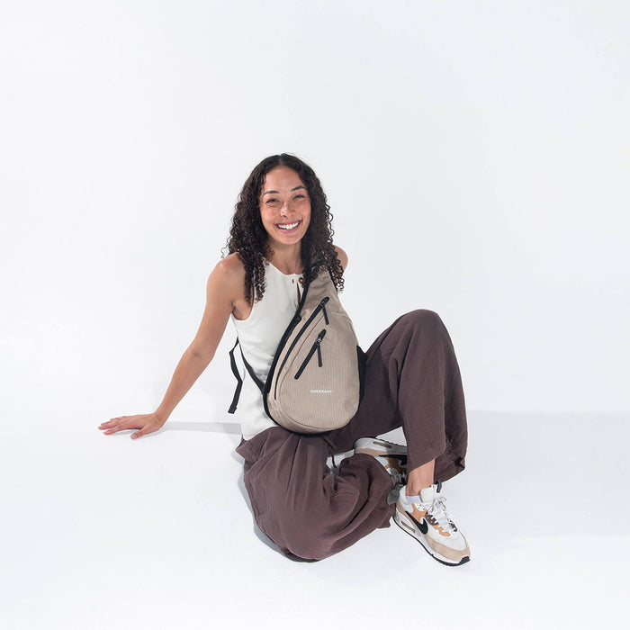 A woman wearing a Sherpani Esprit Straw Beige Anti-theft Sling Bag on her front against a white background. #color_straw-beige