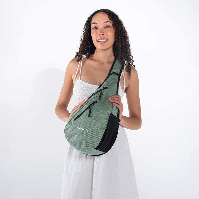 A woman wearing a Sherpani Esprit Aloe Mist Green Anti-theft Sling Bag on her front against a white background. #color_aloe-mist-green