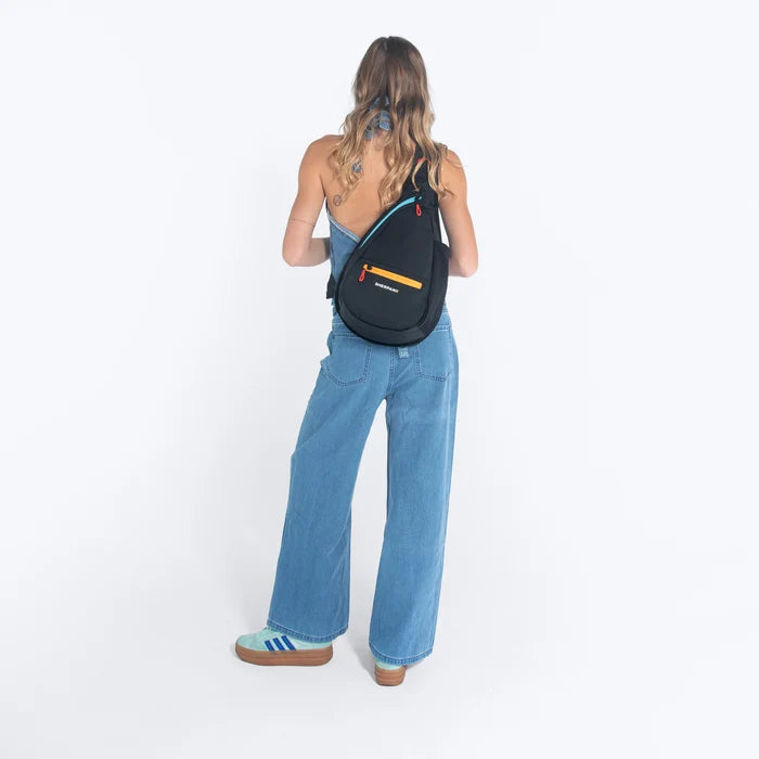 Woman wearing a Sherpani Esprit Chromatic Black Sling on her back against white backdrop. #color_chromatic-black