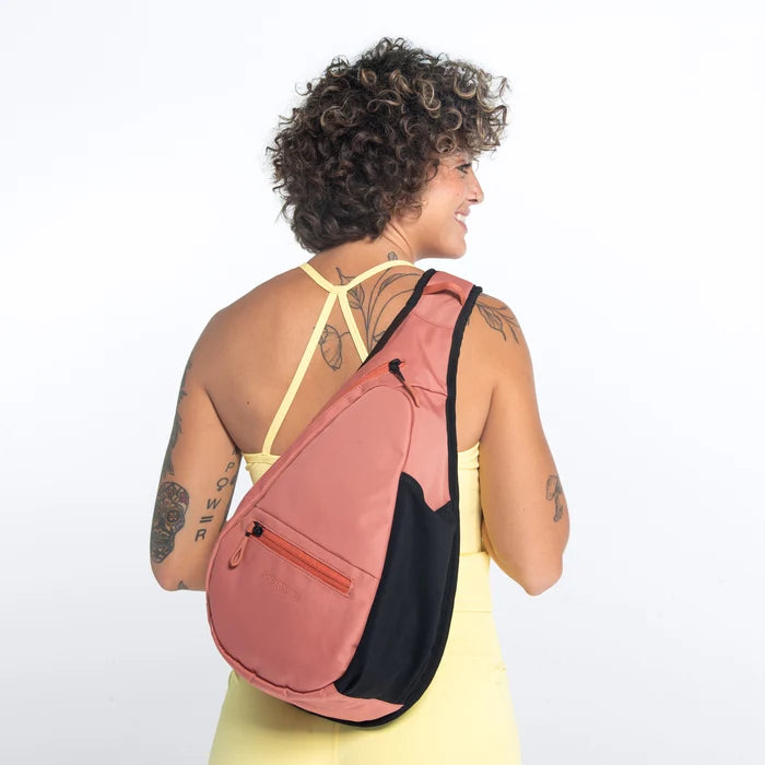 Woman wearing a Sherpani Esprit Desert Pink Sling on her back against white backdrop. #color_desert-pink