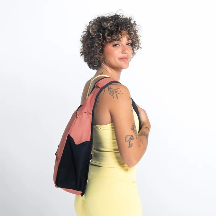 Woman wearing a Sherpani Esprit Desert Pink Sling on her back against white backdrop. #color_desert-pink