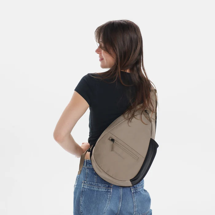 Woman wearing a Sherpani Esprit Dune Sling on her back against white backdrop. #color_dune-tan