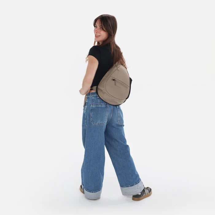 Woman wearing a Sherpani Esprit Dune Sling on her back against white backdrop. #color_dune-tan