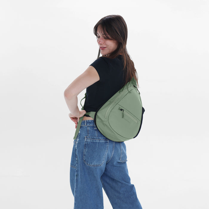 Woman wearing a Sherpani Esprit Olivine Sling on her back against white backdrop. #color_olivine-green
