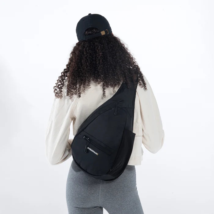 Woman wearing a Sherpani Esprit Raven Black Sling on her back against white backdrop. #color_raven-black