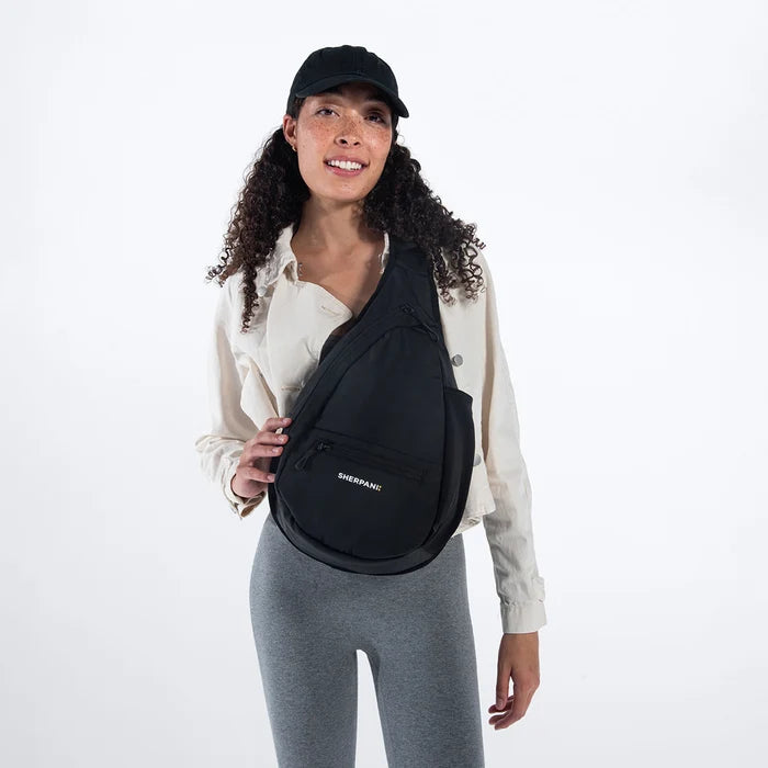 Woman wearing a Sherpani Esprit Raven Black Sling on her front against white backdrop. #color_raven-black
