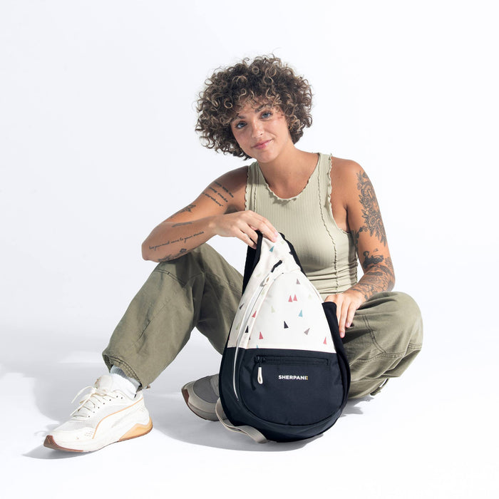 Woman sitting with a Sherpani Esprit Terrazzo Print Sling Bag against white background.  #color_terrazzo-print