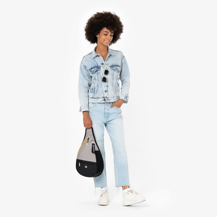 Woman holding a Sherpani Esprit Wasabi Stone Sling Bag by the strap against white background.  #color_wasabi-stone-heritage