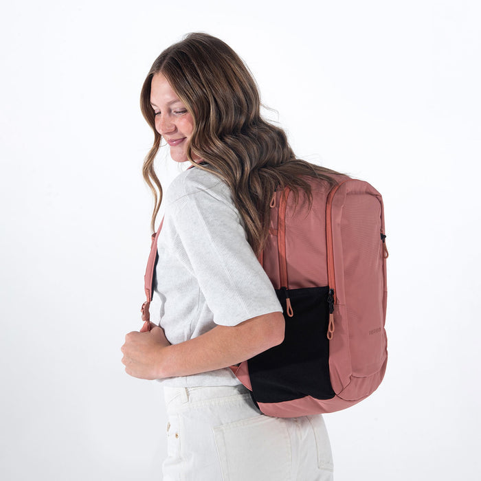 Woman wearing a Sherpani Getaway Desert Pink Travel Backpack on her back against white backdrop.  #color_desert-pink