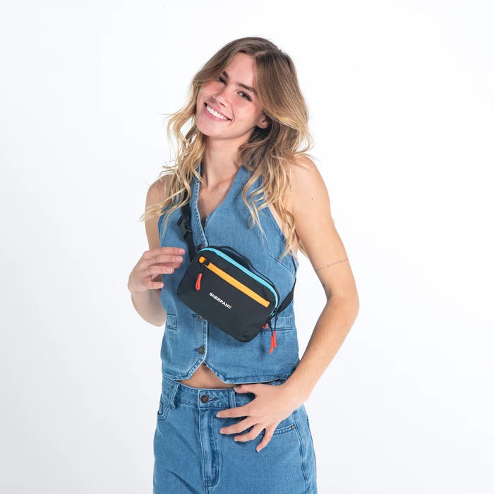 Woman wearing a Sherpani Hyk Chromatic Black Hip Pack across her body against white backdrop.  #color_chromatic-black
