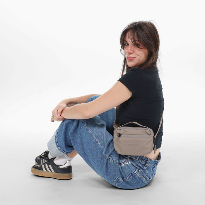 Woman wearing a Sherpani Hyk Dune Hip Pack on her hip against white backdrop.  #color_dune-tan