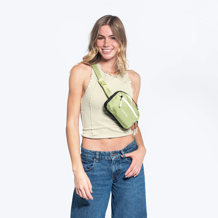 Woman wearing a Sherpani Hyk Palm Green Hip Pack across her body against white backdrop.  #color_palm-green