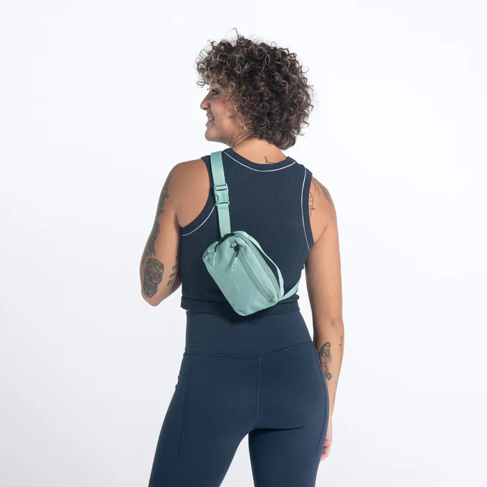 Woman wearing a Sherpani Hyk Surf Blue Hip Pack across her back against white backdrop. #color_surf-blue