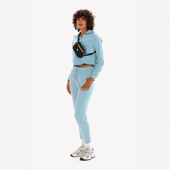 Woman wearing a Sherpani Hyk Chromatic Black Hip Pack across her body against white backdrop. #color_chromatic-heritage