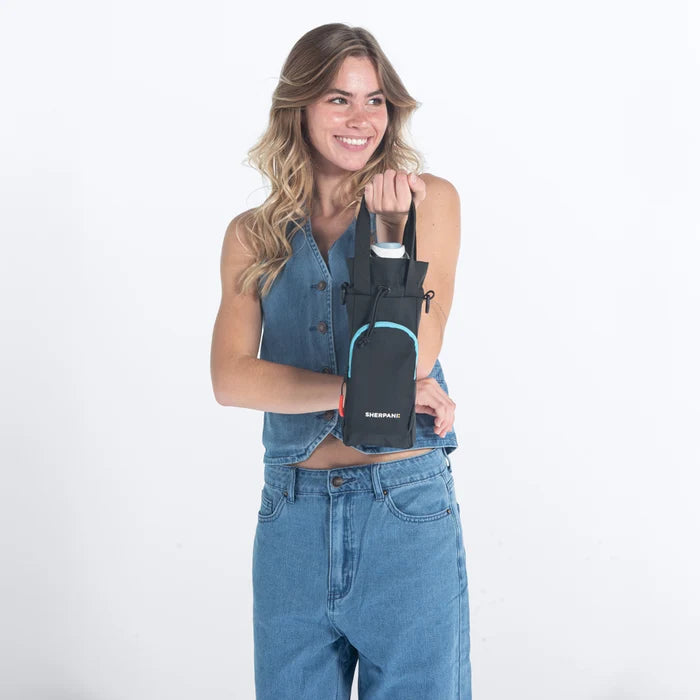 Woman holding a Sherpani Izzie Chromatic Black Water Bottle Crossbody by handheld straps on white background.  #color_chromatic-black
