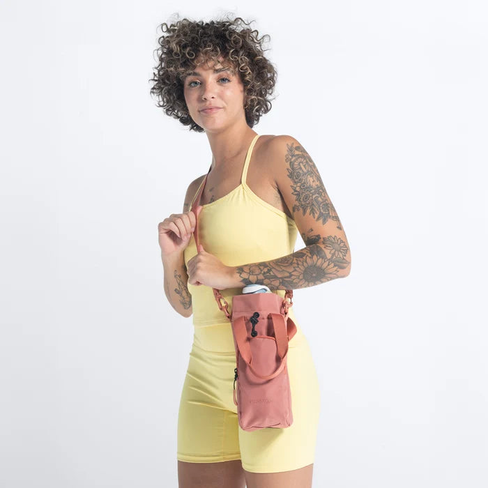 Woman wearing a Sherpani Izzie Desert Pink Water Bottle Crossbody on white background. #color_desert-pink