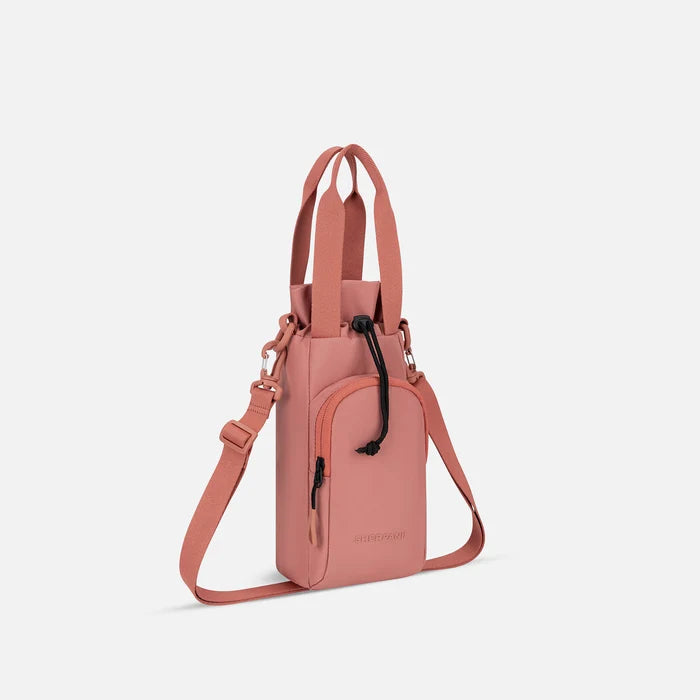 A Sherpani Izzie Desert Pink Water Bottle Crossbody, 3/4 view showing strap and front pocket on white background.  #color_desert-pink
