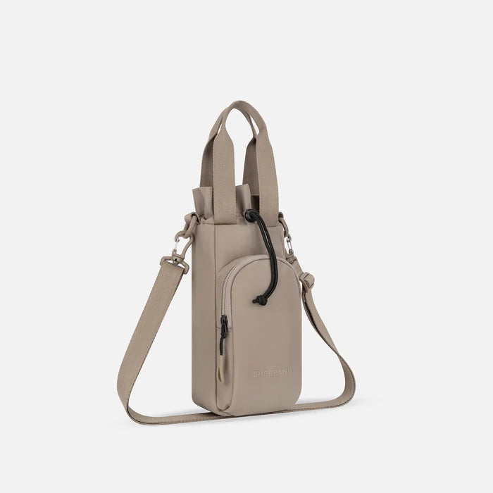 A Sherpani Izzie Dune Water Bottle Crossbody, 3/4 view showing strap and front pocket on white background.  #color_dune-tan