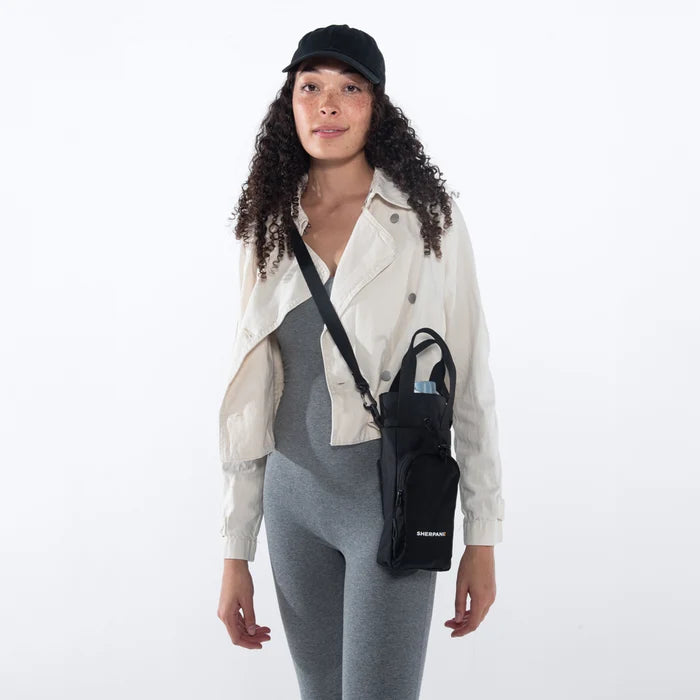 Woman wearing a Sherpani Izzie Raven Black Water Bottle Crossbody on white background.  #color_raven-black
