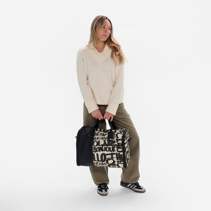 Woman holding a Sherpani Jaunt Ciao  Garment Duffle against white backdrop. #color_ciao-print