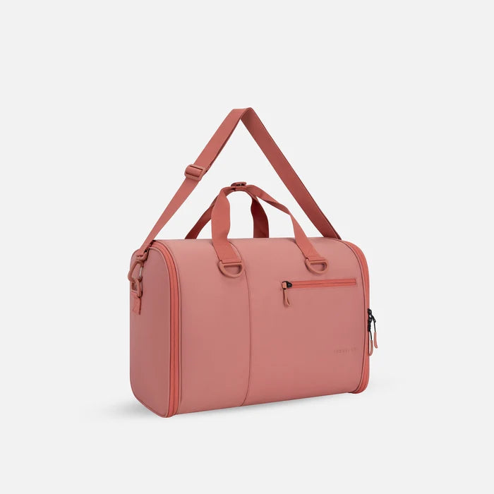 A Sherpani Jaunt Desert Pink Garment Duffle, 3/4 view showing two strap options on white backdrop. #color_desert-pink