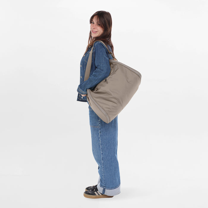 Woman wearing a Sherpani Jaunt Dune Tan Garment Duffle by the crossbody strap against white backdrop #color_dune-tan