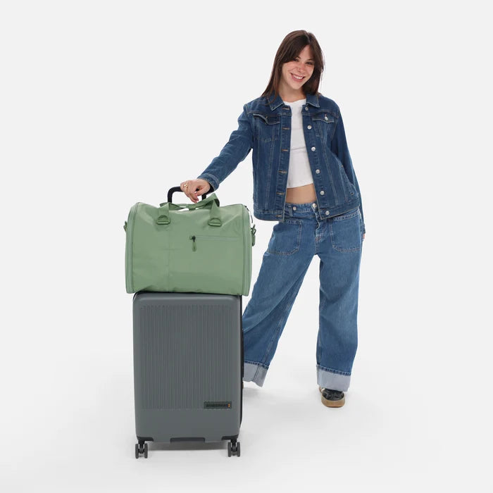 A woman holding Sherpani Jaunt Olivine Garment Duffle on top of a Sherpani Meridian Luggage. #color_olivine-green