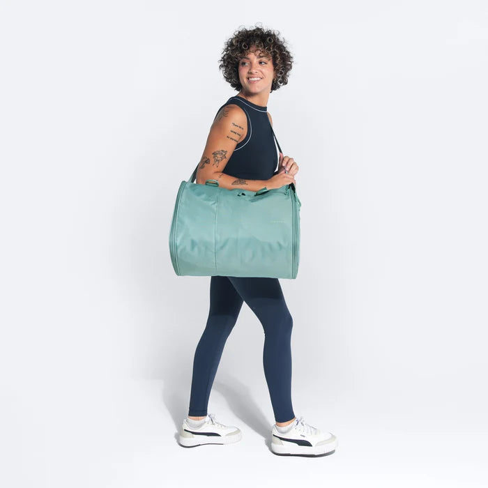 Woman wearing a Sherpani Jaunt Surf Blue Garment Duffle by the crossbody strap against white backdrop #color_surf-blue