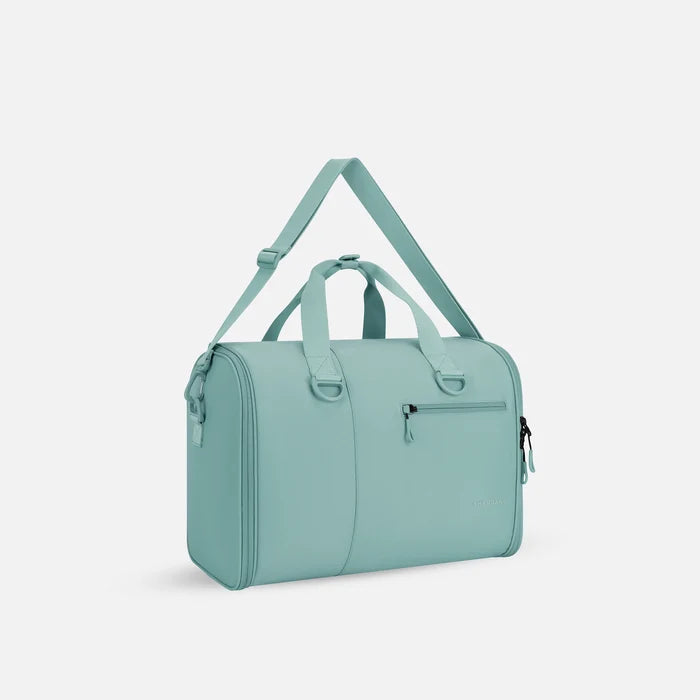 A Sherpani Jaunt Surf Blue Garment Duffle, 3/4 view showing two strap options on white backdrop. #color_surf-blue