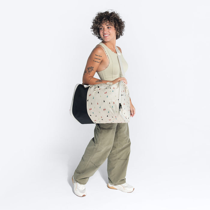 Woman wearing a Sherpani Jaunt Terrazzo Print Garment Duffle by long strap against white backdrop. #color_terrazzo-print