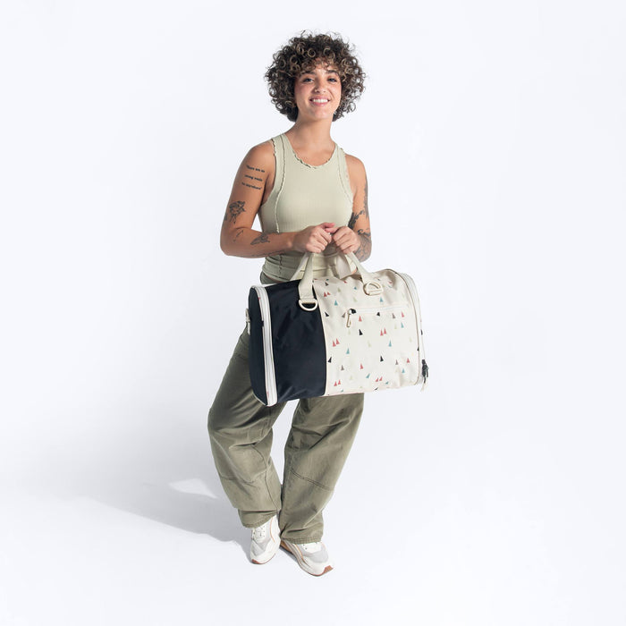 Woman holding a Sherpani Jaunt Terrazzo Print Garment Duffle by top straps against white backdrop. #color_terrazzo-print