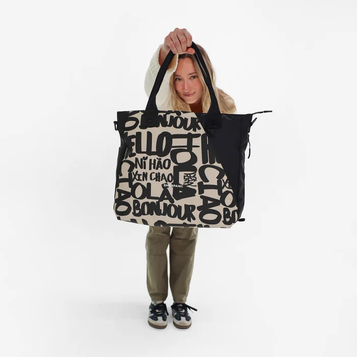 A woman holding a Sherpani Jetsetter Ciao Travel Tote Bag on white backdrop. #color_ciao-print
