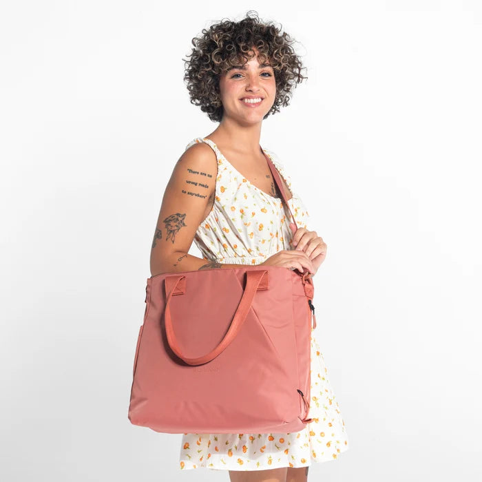 A woman wearing a Sherpani Jetsetter Desert Pink Travel Tote Bag on white backdrop.  #color_desert-pink